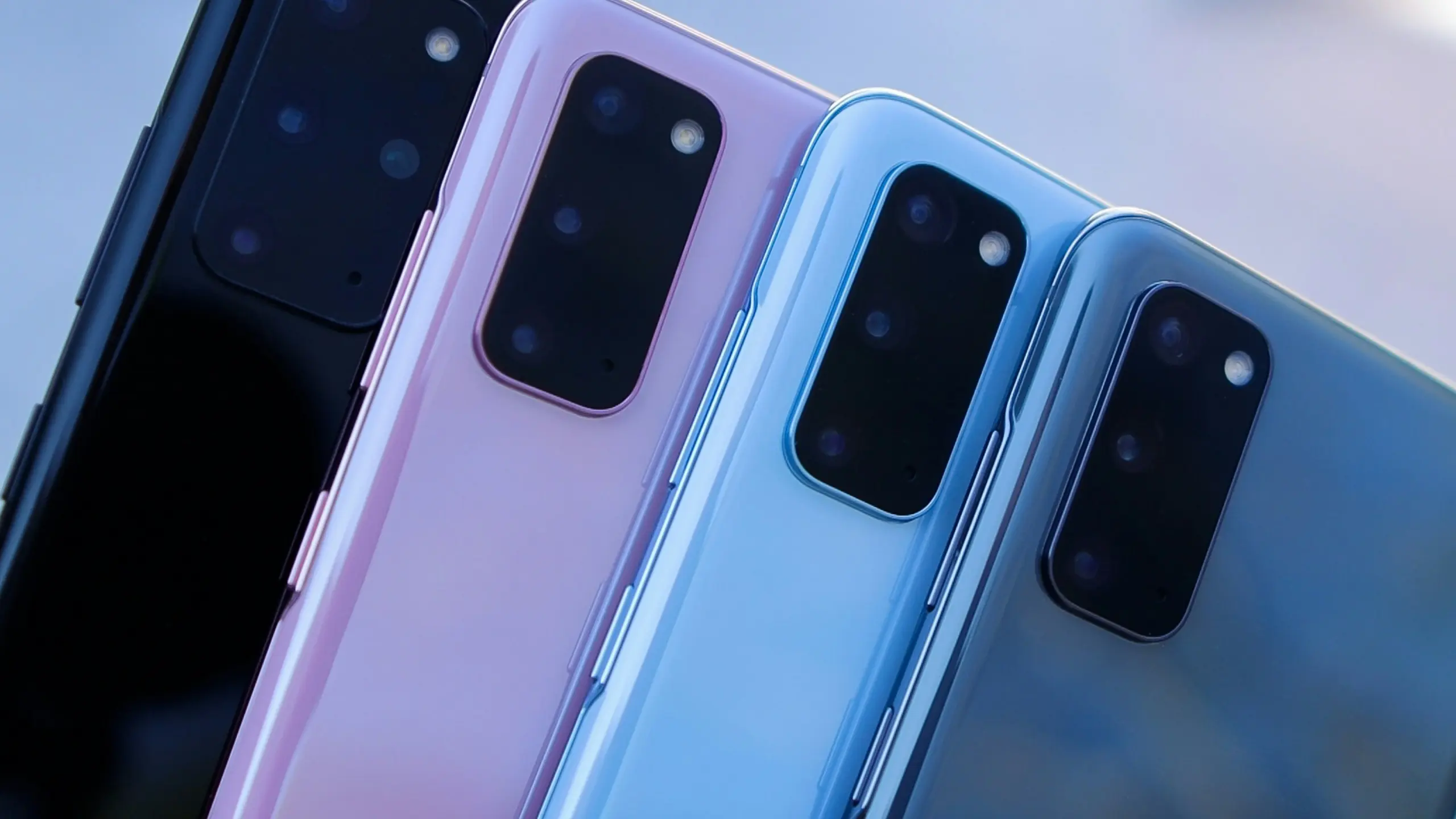 Back view of multiple smartphones in pink and blue finishes, showing large rectangular camera bumps and lenses grouped together in a diagonal row.