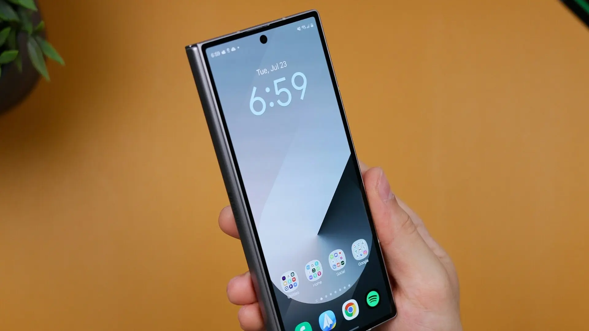 Hand holding a modern smartphone with edge-to-edge display and app icons on the home screen against an orange background.