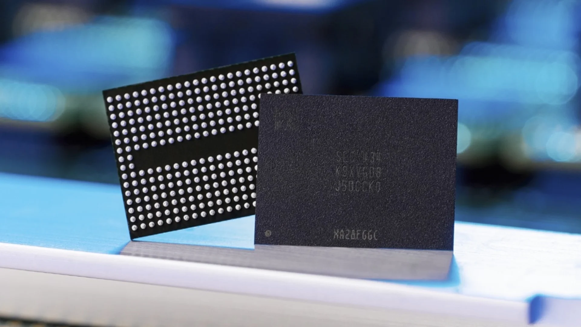 Two computer chips standing upright on a blue surface: a dense ball-grid array (BGA) chip and a dark square processor beside it.