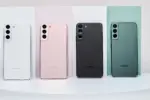 Four Samsung smartphones shown from the back in white, pink, black, and green, standing on pastel panels on a white surface.