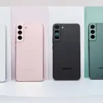 Four Samsung smartphones shown from the back in white, pink, black, and green, standing on pastel panels on a white surface.