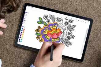 Tablet on carpet, hand using a stylus to color a floral design in a digital coloring app; color palette along the edge is visible.
