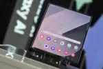 Foldable smartphone on a display stand, with a home screen full of colorful app icons and a weather widget.