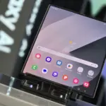 Foldable smartphone on a display stand, with a home screen full of colorful app icons and a weather widget.