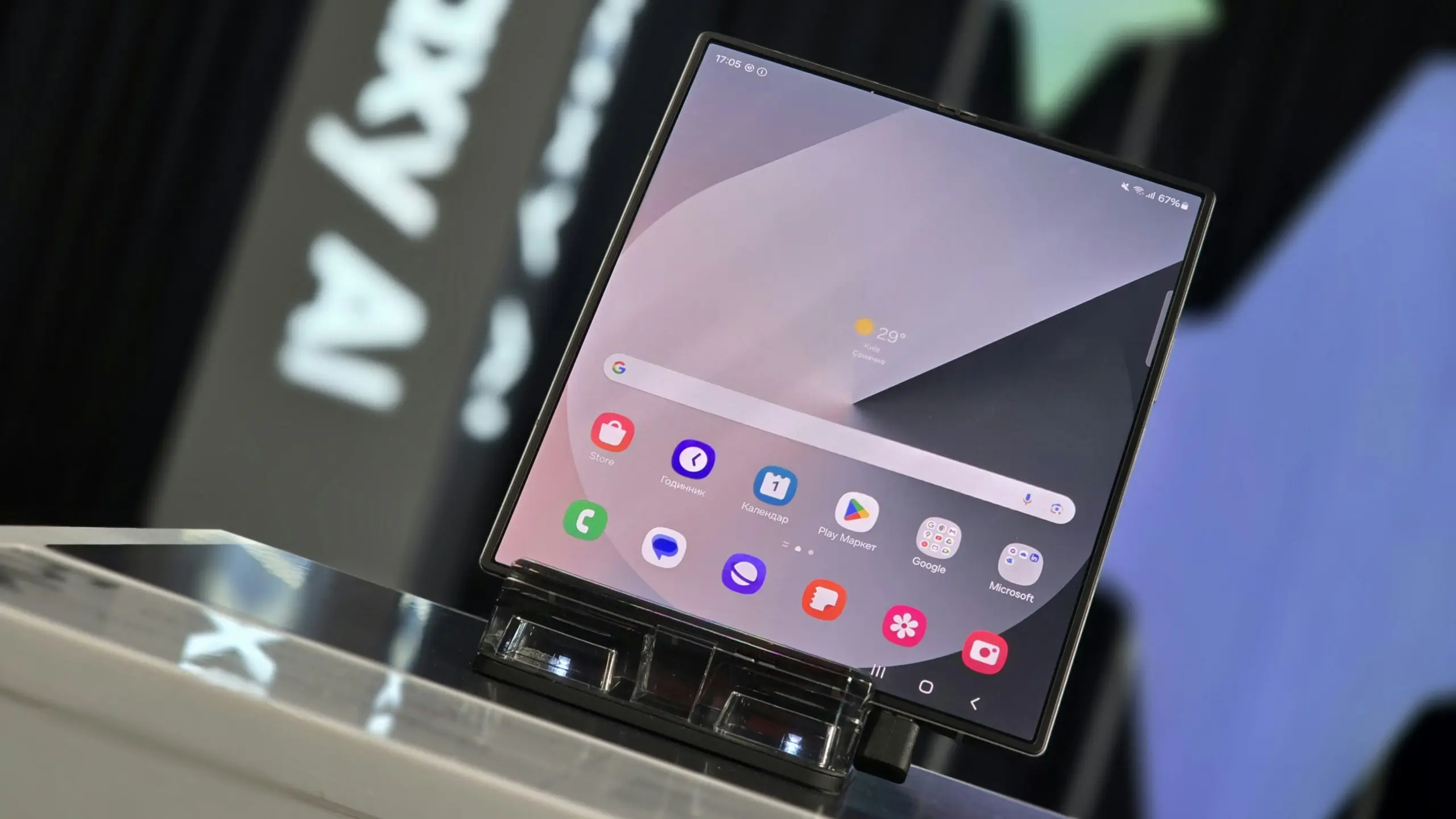 Foldable smartphone on a display stand, with a home screen full of colorful app icons and a weather widget.