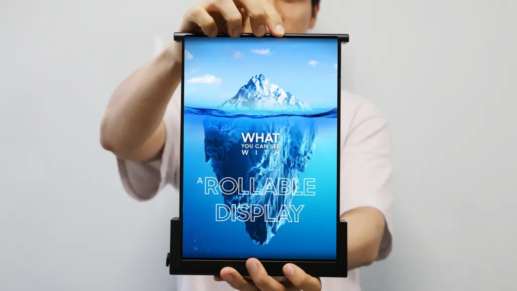 Person holding a tall rollable display showing an iceberg image and the words 'What you can see with a rollable display' on the screen.