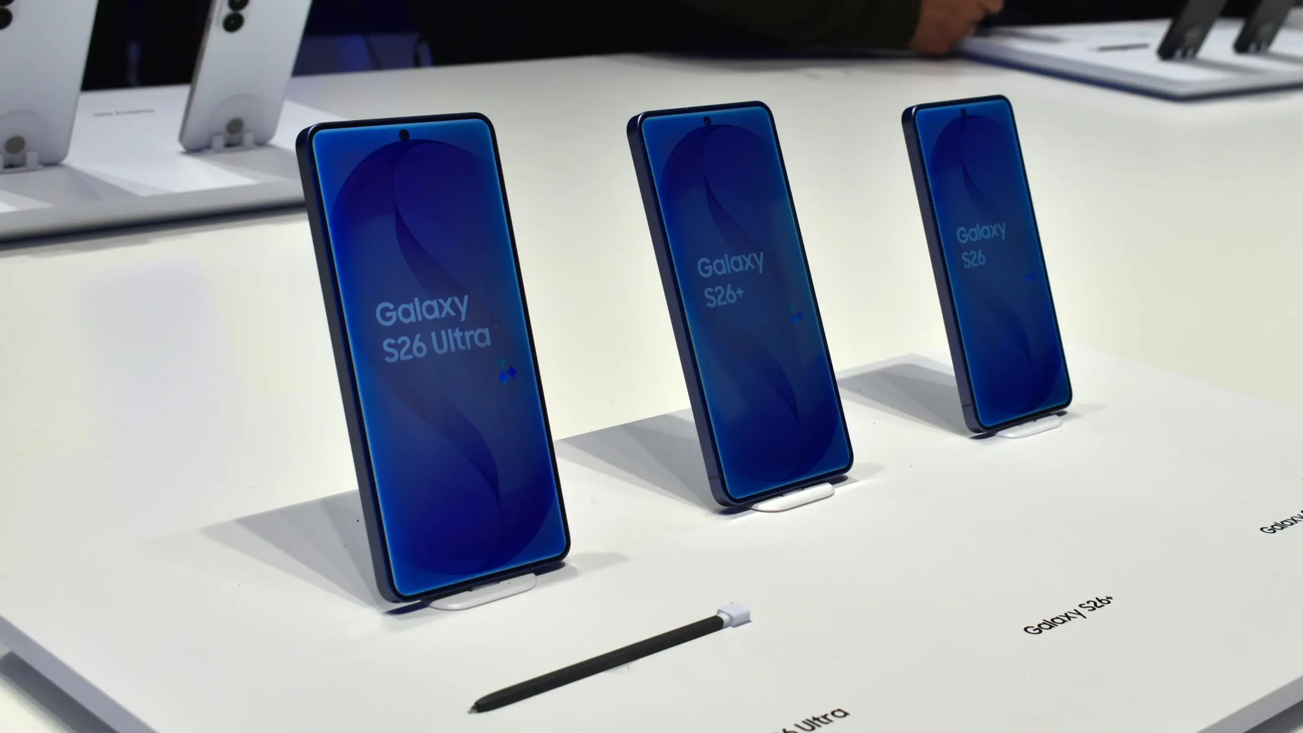 Row of blue Galaxy S26 Ultra/S26+/S26 smartphones on angled display stands in a bright showroom.