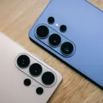Two smartphones with multiple rear cameras on a wooden surface, showing large circular camera lenses arrayed in groups.