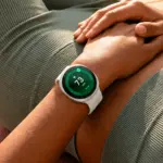 Close-up of a person wearing a white smartwatch showing heart rate 73 bpm on a green screen, resting hands on knee outdoors.