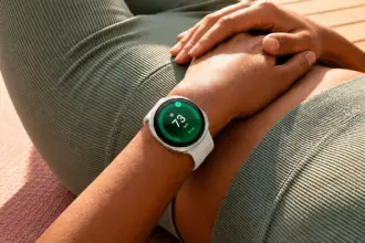 Close-up of a person wearing a white smartwatch showing heart rate 73 bpm on a green screen, resting hands on knee outdoors.