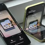Two Galaxy Flip foldable smartphones in green and gold sit on a light surface, screens showing a FlexCam promo and Cyrillic text.