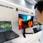 Man in a white shirt examining a row of gaming displays at a showroom wall