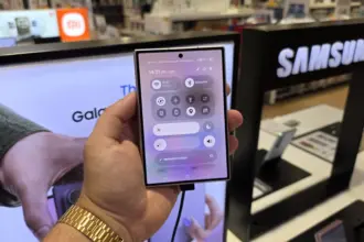 Hand holding a smartphone showing quick settings (Wi‑Fi, Bluetooth) on the screen in a Samsung store display background.