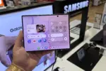 Person holds a Samsung Galaxy foldable phone displaying app icons and control panel in a store display area