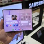 Person holds a Samsung Galaxy foldable phone displaying app icons and control panel in a store display area
