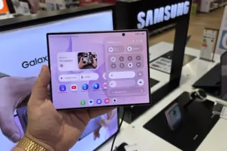 Person holds a Samsung Galaxy foldable phone displaying app icons and control panel in a store display area