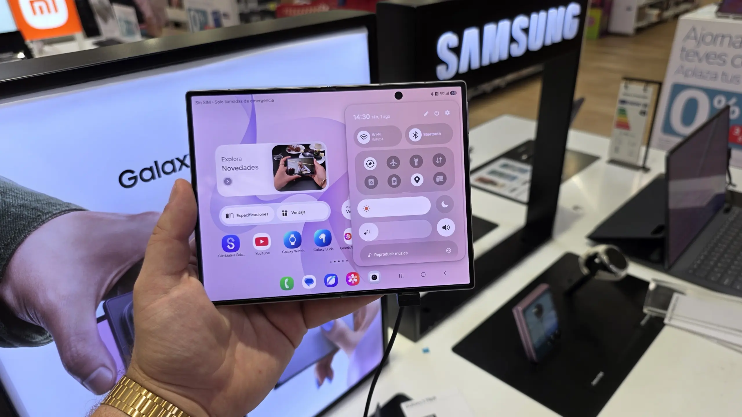 Person holds a Samsung Galaxy foldable phone displaying app icons and control panel in a store display area